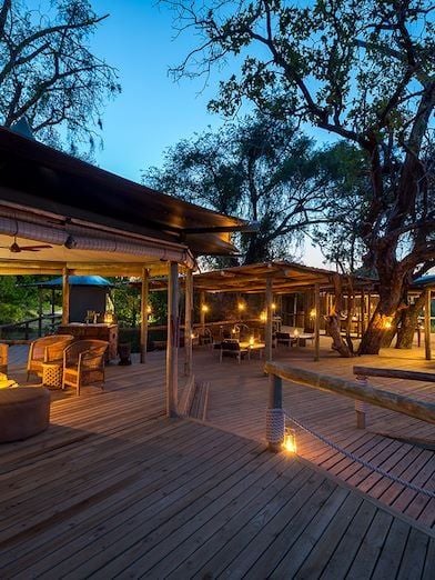 Luxurious safari tented suite overlooking Botswana's lush wilderness, with elegant wooden deck, canvas walls, and panoramic savanna views at sunset