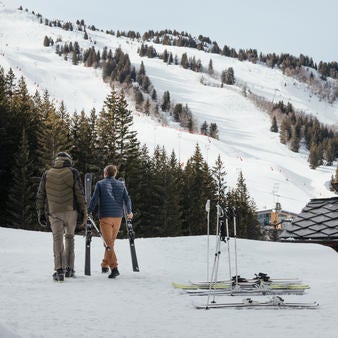 Elegant ski-in ski-out hotel with wooden balconies and snow-covered facade nestled in French Alps, surrounded by snow-laden pine trees