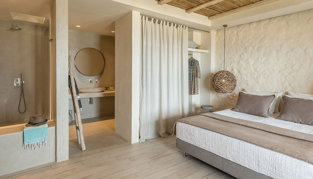 White-washed Cycladic hotel room with minimalist design, blue accents, private balcony overlooking Sifnos island's azure Aegean Sea landscape at sunset