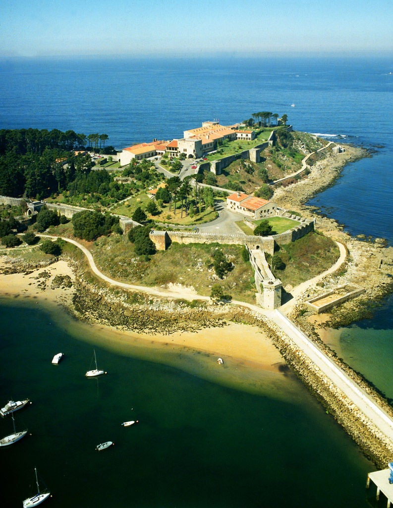 Historic stone fortress hotel Parador de Baiona perched on rocky peninsula overlooking Atlantic Ocean, featuring elegant towers and gardens