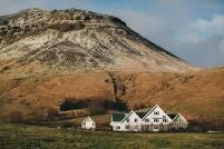 Luxurious Icelandic manor hotel with traditional turf-roofed architecture, nestled in verdant landscape with dramatic mountains and lush green countryside