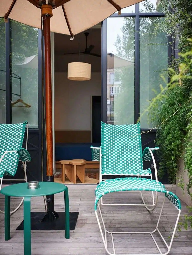 Sunlit Barcelona hotel terrace with lush greenery, mid-century modern furniture, and chic urban design overlooking a charming interior courtyard