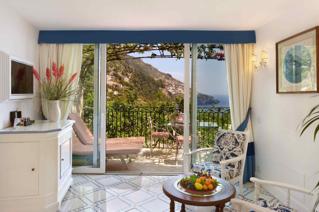 Luxury cliffside hotel in Positano with Mediterranean balconies cascading down rocky coast, overlooking turquoise Amalfi waters at sunset