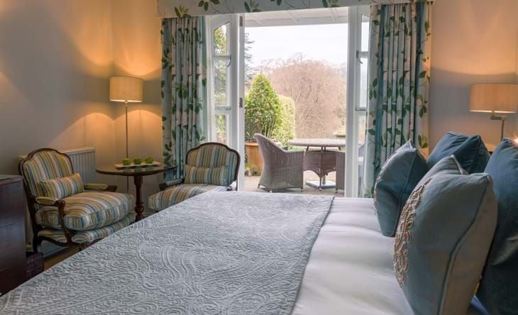 Luxurious garden-view room at scenset-renowned Chewton Glen Hotel & Spa, featuring elegant decor, plush bedding, and expansive windows overlooking lush greenery in the United Kingdom.