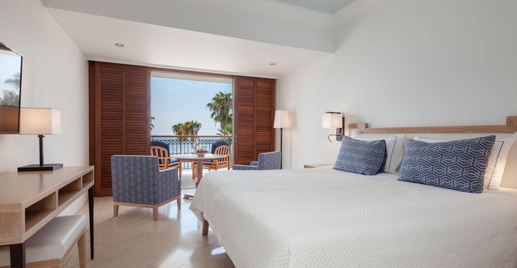 Elegant deluxe sea view room with modern decor, plush king bed, floor-to-ceiling windows overlooking azure Mediterranean coastline in Cyprus