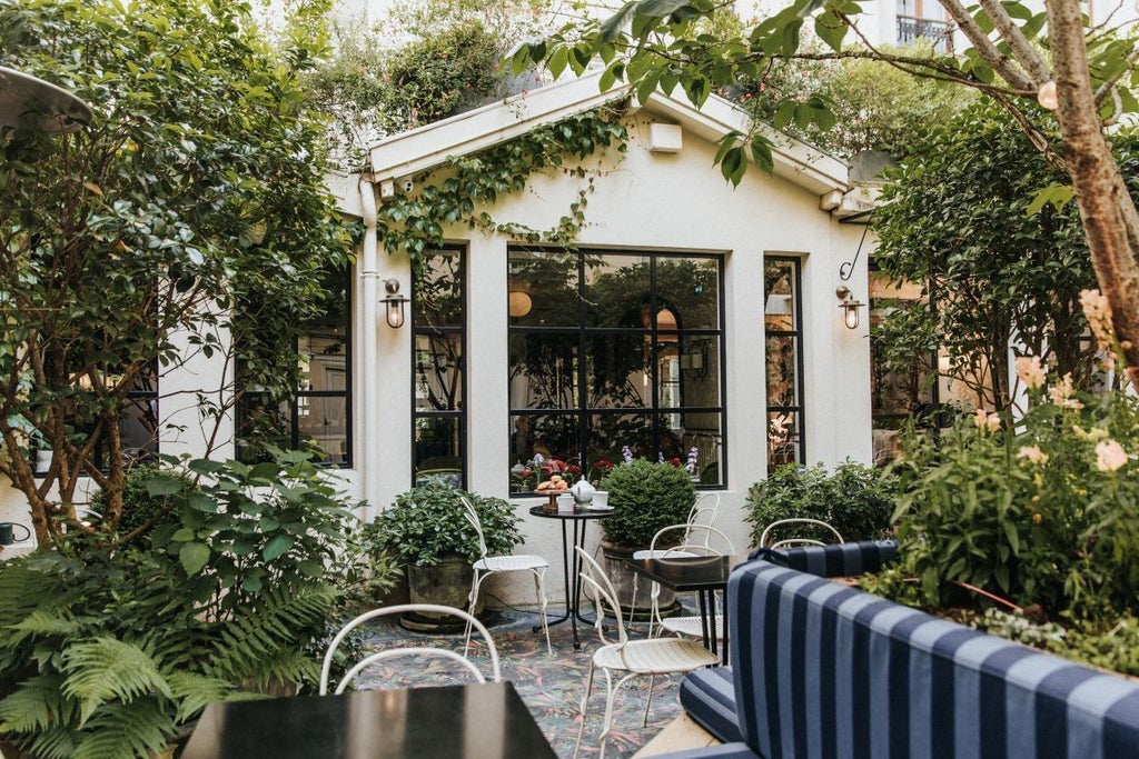 Elegant Parisian boutique hotel facade with soft pastel pink exterior, ornate wrought-iron balconies, and charming traditional French architectural details