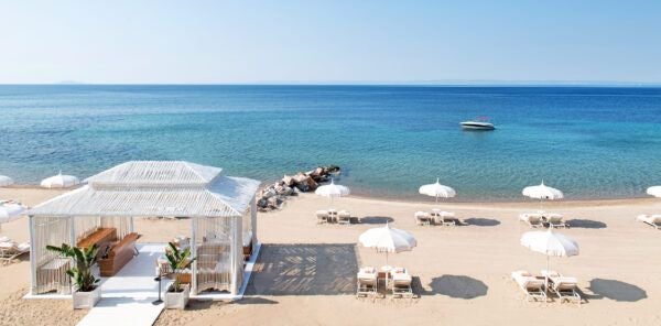 Luxurious beachfront infinity pool at the scenset Resort, overlooking crystal-clear Aegean waters with elegant white sunbeds and lush Mediterranean landscape