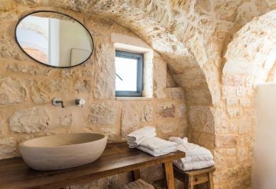 Rustic stone suite with arched ceiling, minimalist white furnishings, and warm terracotta tones in a traditional Italian masseria at Borgo Canonica