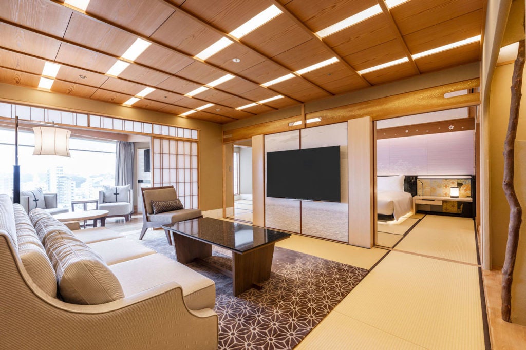 Elegant Japanese hotel exterior with traditional curved roof, stone lanterns, cherry blossoms and modern glass entrance at dusk