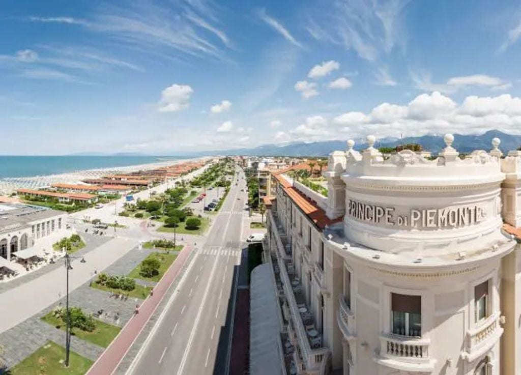 Elegant five-star hotel facade with ornate Art Deco architecture, classical columns, and wrought-iron balconies overlooking the Italian coast