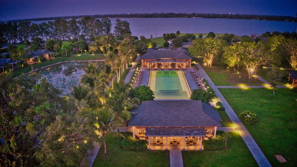 Modern resort bungalows nestled among tropical trees along a tranquil river, featuring elegant wooden architecture and private terraces