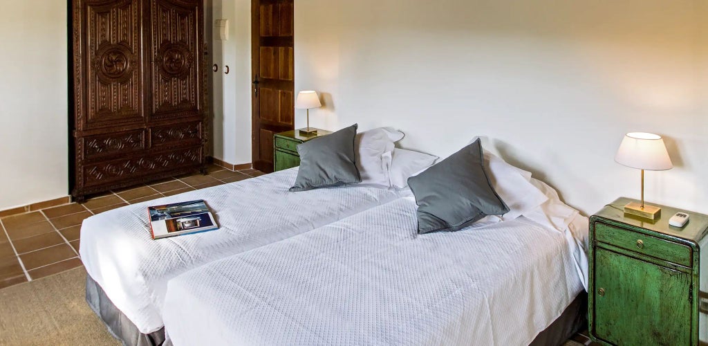 Elegant Spanish country hotel room with rustic wooden furniture, white linens, and panoramic views of rolling olive groves and mountainous landscape.