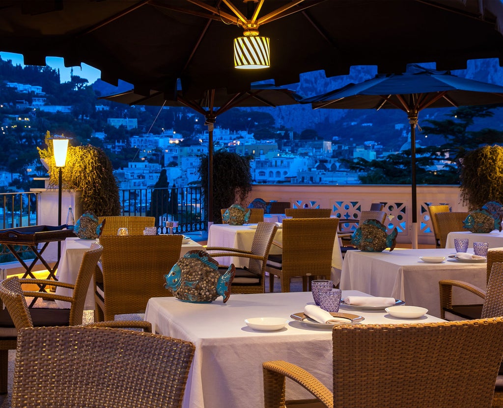 Elegant Mediterranean-style hotel with white facades and blue accents, featuring a luxurious terrace overlooking Capri's coastline