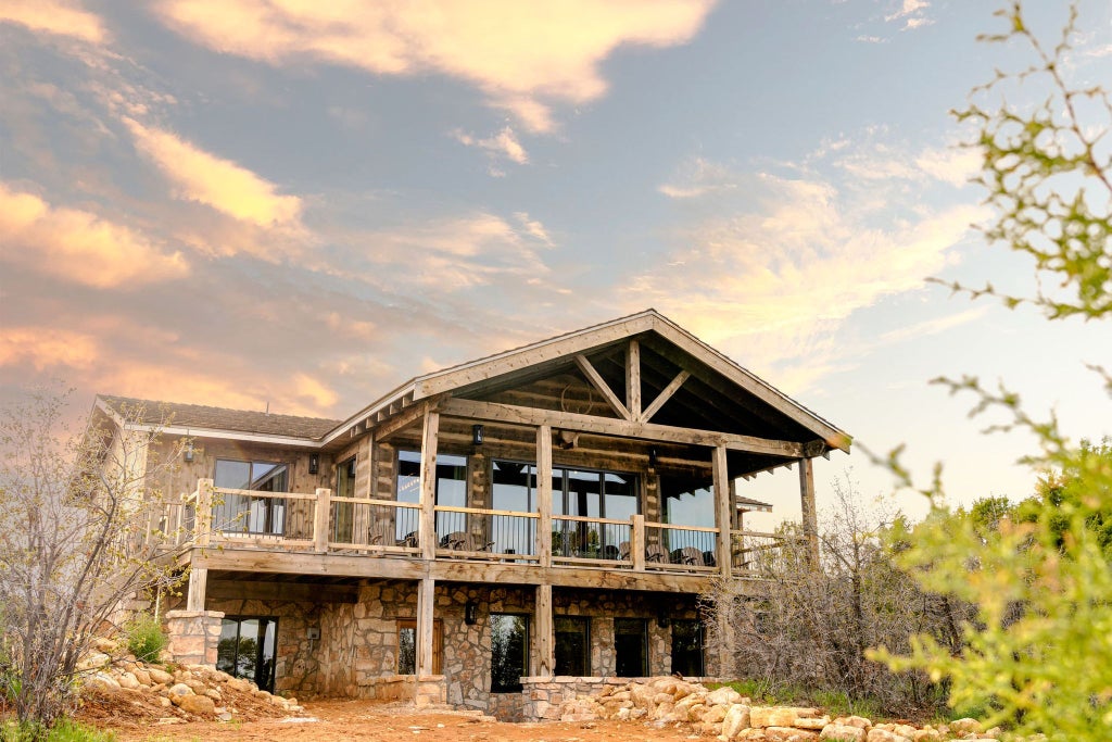 Rustic lodge room with wooden furnishings, plush bed, and large window overlooking scenic mountain landscape at Scenset Mountain Ranch in southwestern United States