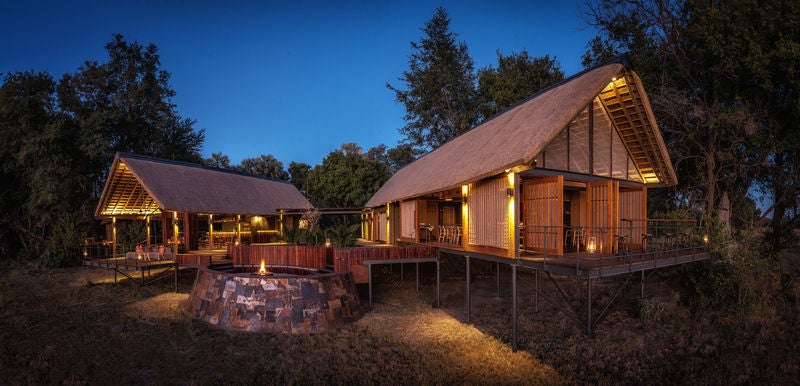 Elevated luxury safari tent overlooking a tranquil delta, with wooden deck, outdoor seating, and canvas walls amid lush African bush