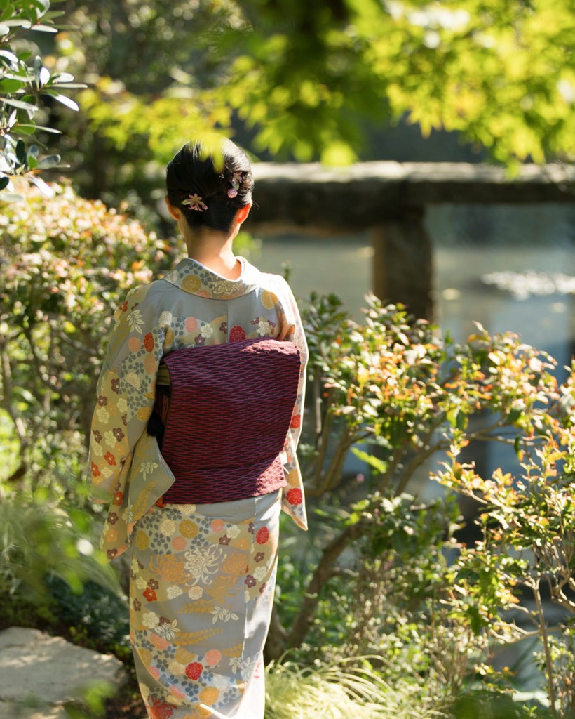 Sunlit interior courtyard of Four Seasons Kyoto featuring traditional Japanese garden with stone path, koi pond and maple trees