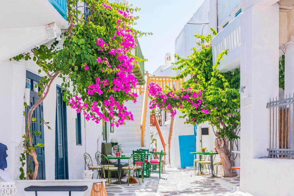 Pristine whitewashed buildings with blue domes cascade down hillside towards crystal-clear Aegean Sea, classic Mykonos architecture