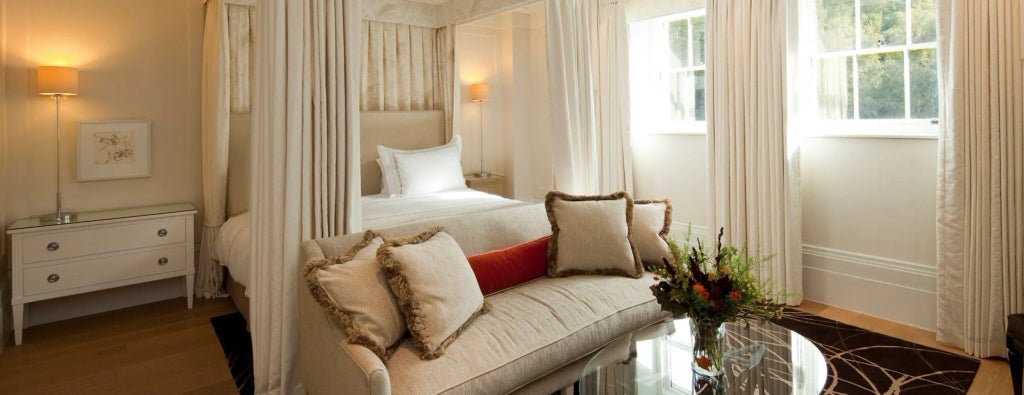 Elegant Deluxe Room at Coworth Park's Mansion House with refined decor, plush king bed, soft neutral tones, and expansive windows overlooking lush grounds