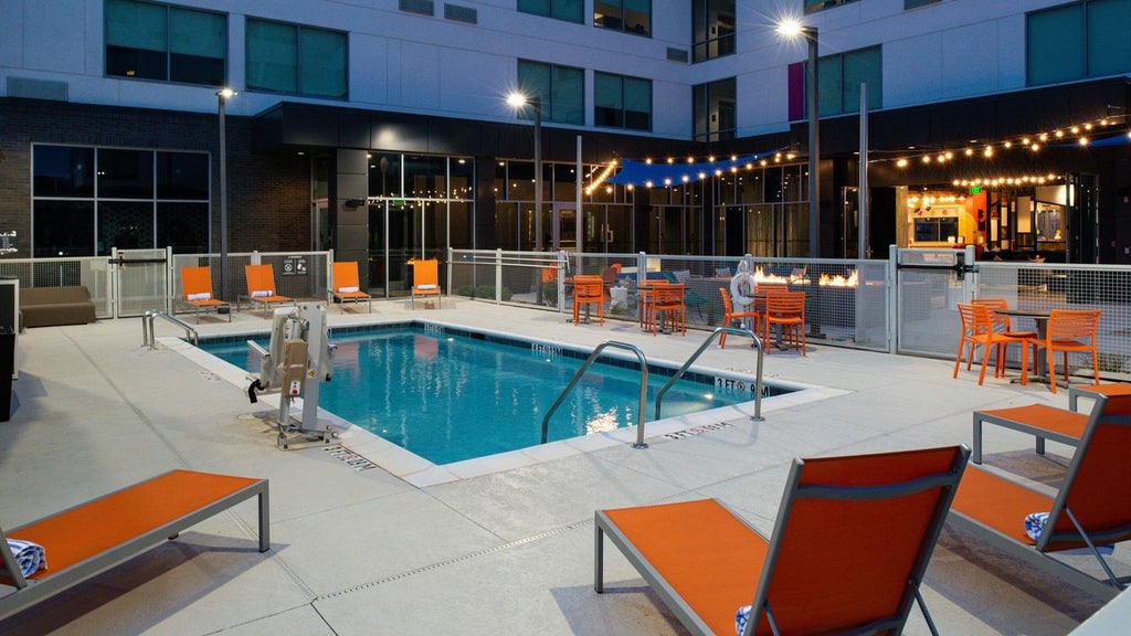 Modern glass-fronted Aloft hotel near airport with sleek architectural design, illuminated lobby, and contemporary urban landscaping at dusk