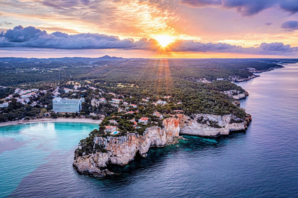 Panoramic view of Menorca's pristine turquoise bay with luxury yachts anchored near white sandy beach and traditional buildings