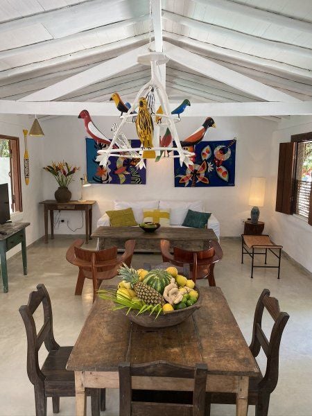 Rustic-chic Brazilian hotel room with wooden floors, white bedding, natural textures, and warm sunlight filtering through traditional tropical-style windows