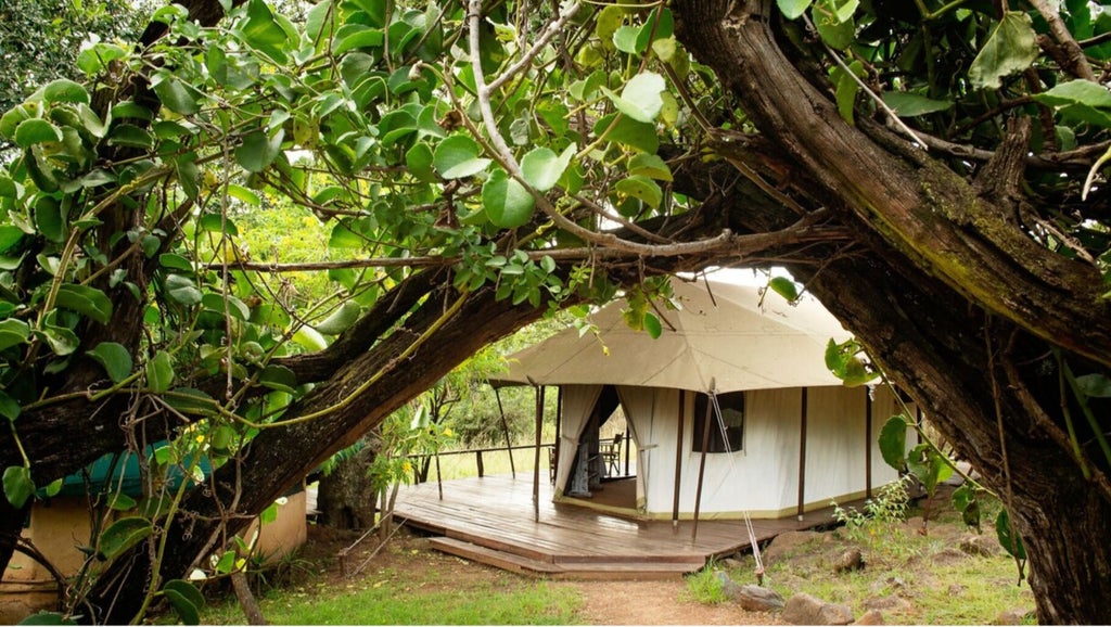 Large canvas safari tent overlooking African savanna, featuring elegant colonial-style furnishings and private veranda with panoramic views