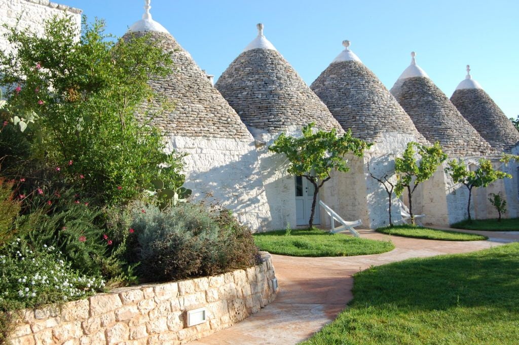 Rustic stone Masseria Cervarolo hotel nestled in Puglia's olive groves, featuring warm ochre walls, traditional architecture, and lush Mediterranean landscape.