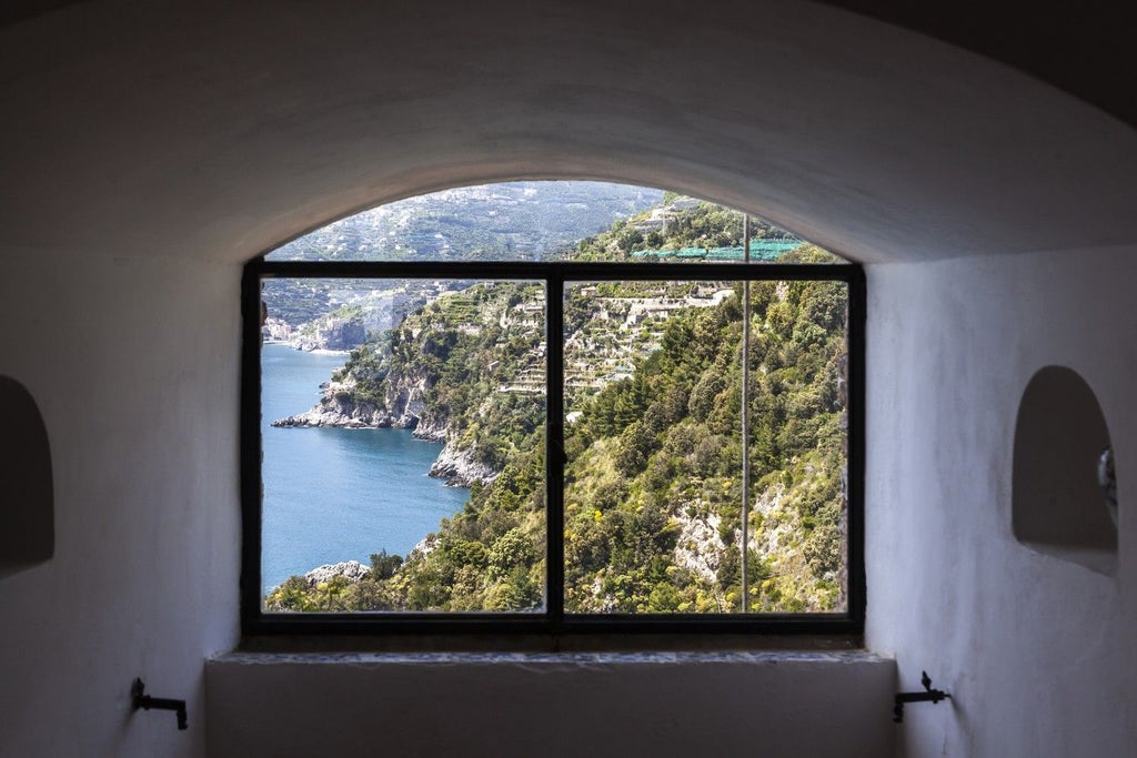 Cliffside medieval watchtower villa with lush Mediterranean gardens cascading to sea, featuring elegant antique-filled living