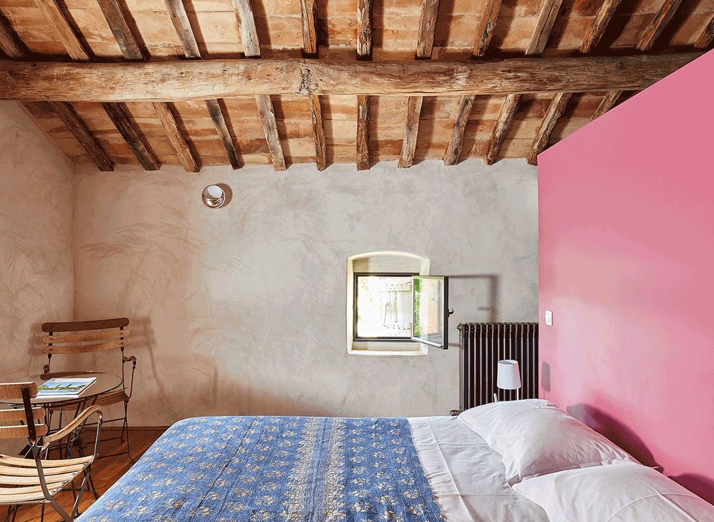 Elegant stone-walled suite with soft blue decor, plush white bedding, antique wooden furniture, and large windows overlooking French countryside landscape