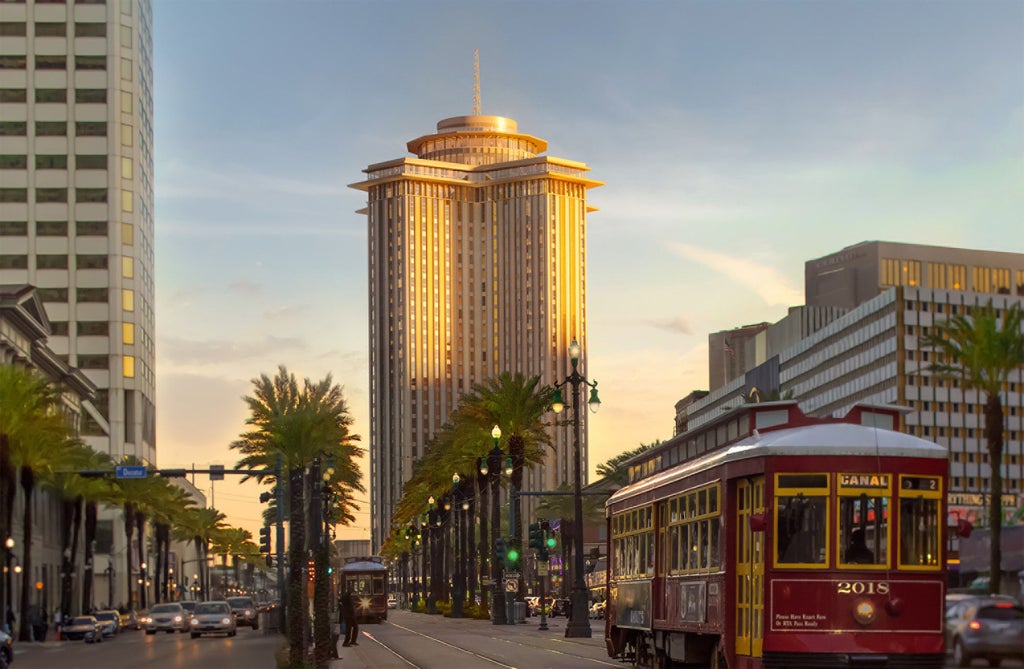 Modern 34-story glass skyscraper hotel on Mississippi River waterfront with curved facade, palm trees and luxury entrance pavilion