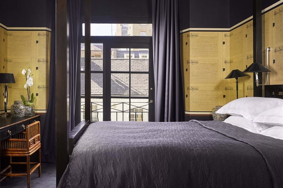 Luxurious double bedroom at a boutique hotel with rich dark wood furniture, elegant textiles, and moody atmospheric lighting in muted tones