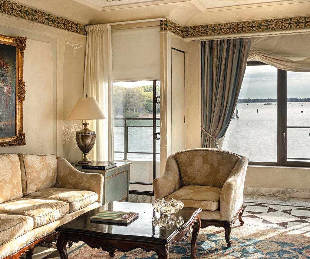 Opulent hotel suite with marble columns, period furniture, silk drapes, and French doors opening to a private balcony with Venice lagoon views