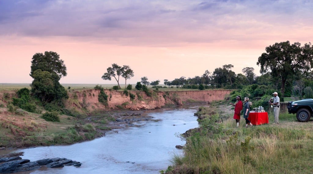 Luxurious safari tent with private deck overlooking the Masai Mara savanna, framed by acacia trees at golden hour sunset