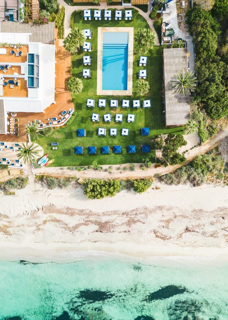 Luxurious beachfront resort with minimalist white architecture, turquoise infinity pool, and panoramic Mediterranean coastline near coastal town.