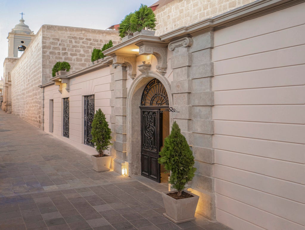 Historic stone hotel with arched colonial windows, rustic white walls, and ornate iron balconies in downtown Arequipa, Peru at sunset