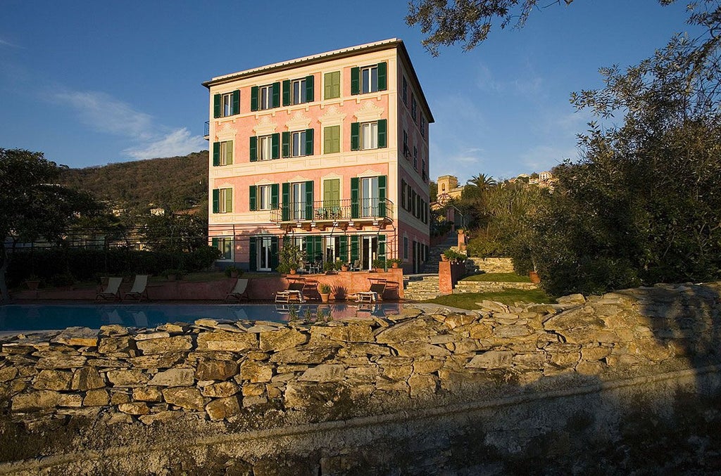 Elegant Italian villa nestled in lush Tuscan landscape, stone facade adorned with rosemary, terracotta roof, and inviting blue-green shutters against verdant hills