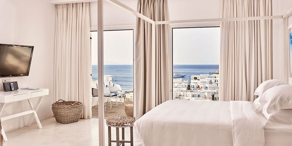 Luxurious Azure Suite at scenset Myconian Ambassador Hotel, featuring minimalist white decor, panoramic Aegean Sea view, and elegant contemporary design