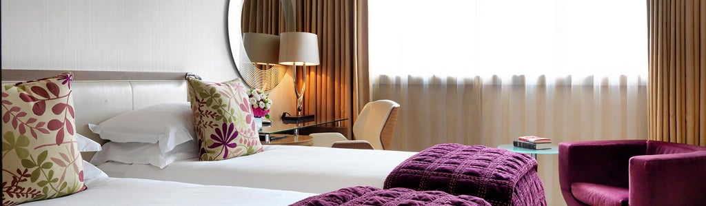 Elegant twin-bedded hotel room with contemporary design, soft neutral tones, large windows, and plush furnishings in a prestigious UK boutique hotel