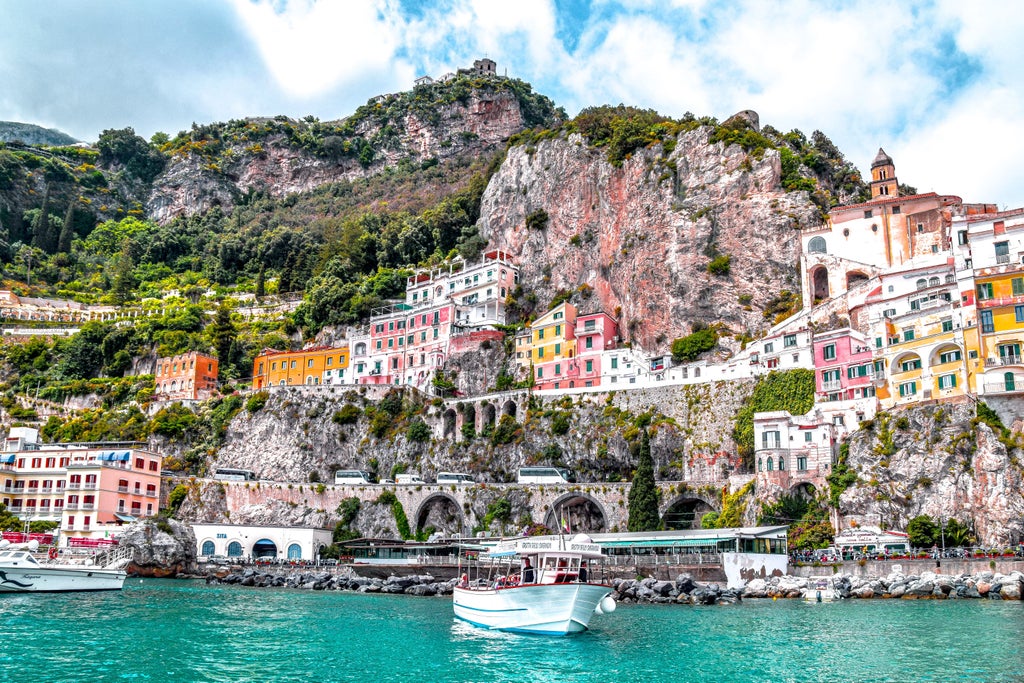 Elegant wooden yacht gliding along Amalfi Coast's turquoise waters, with dramatic cliffs and pastel-colored villages perched above