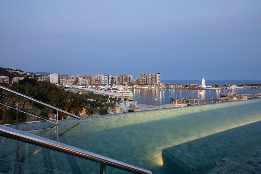 Modern luxury hotel exterior at dusk, featuring illuminated glass windows, contemporary architecture and stylish white facade in downtown Malaga