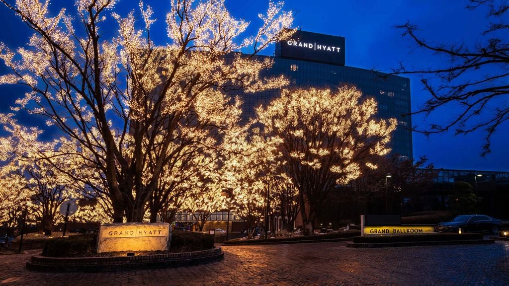 Modern luxury hotel tower with glass facade reflects city lights, nestled among green hills overlooking Seoul's skyline at dusk