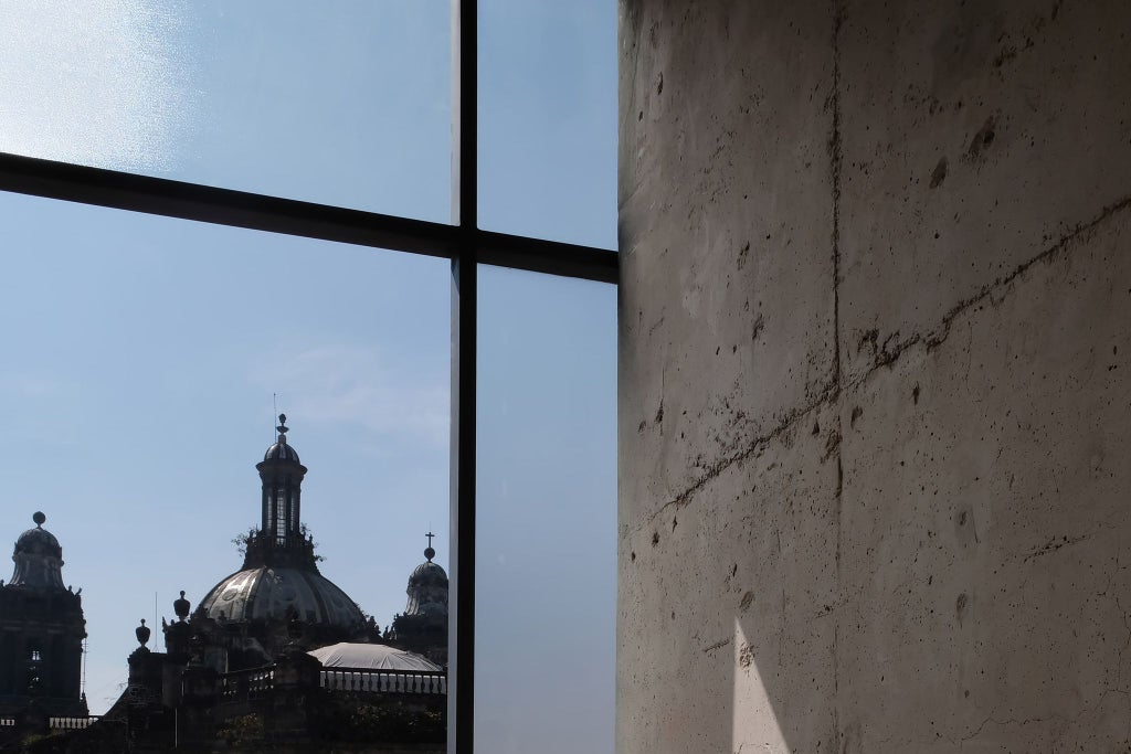 Elegant minimalist hotel courtyard with stone walls, arched walkways, and a central water feature, showcasing Mexican architectural design in soft natural light