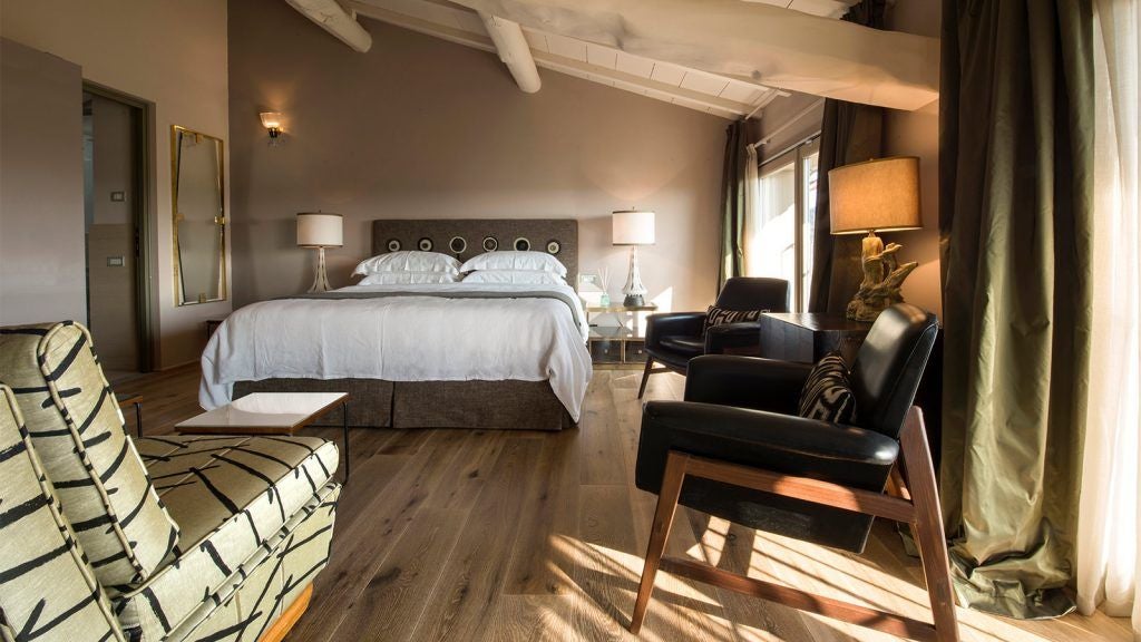 Elegant Tuscan hotel room with soft white linens, wooden floors, and large windows overlooking rolling countryside landscapes near [location will be provided]