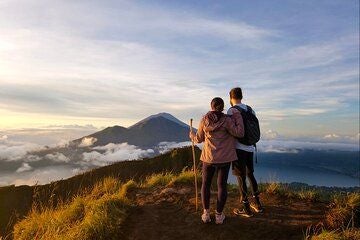 Majestic sunrise illuminating Mount Batur's volcanic landscape, silhouetted hikers ascending rocky trail with misty Indonesian mountainscape in background