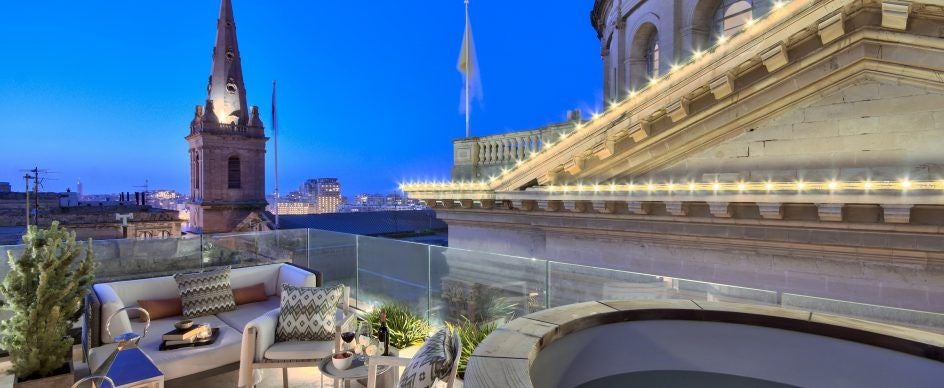 Elegant boutique hotel facade in Malta with limestone walls, arched windows, and lush greenery, showcasing historic Mediterranean architectural charm