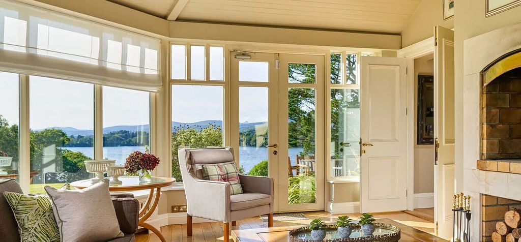 Bright, elegant cottage bedroom featuring a king bed with crisp white linens, French doors opening to garden views, and refined decor