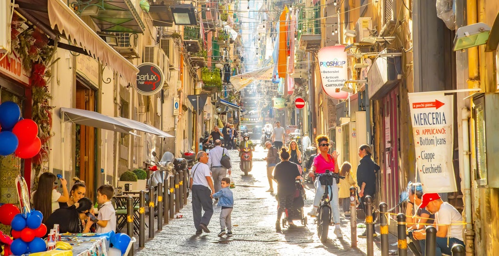 Small group enjoying authentic Neapolitan pizza and wine at traditional restaurant in Naples, with colorful coastal views nearby