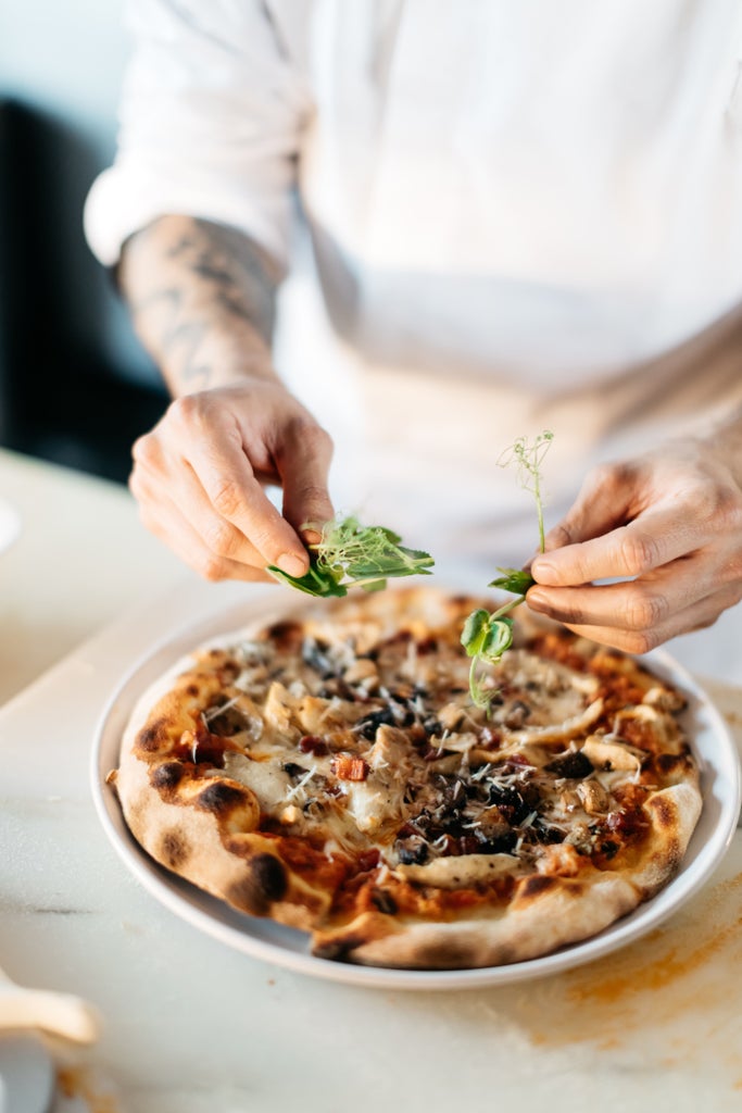 Artisanal pizza dough being stretched by hands on marble countertop, dusted with flour, in a rustic Tuscan cooking studio