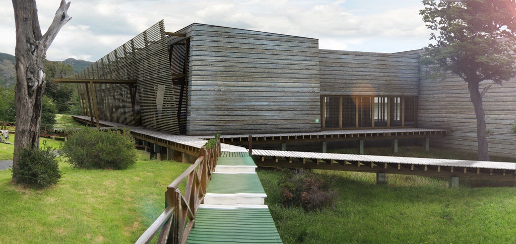 Upscale mountain lodge with floor-to-ceiling windows overlooking Grey Lake and snow-capped Torres del Paine peaks at sunset in Patagonia