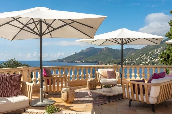 Luxurious seaside hotel with Mediterranean blue waters, white-washed terrace, and elegant stone architecture overlooking French Riviera coastline at sunset